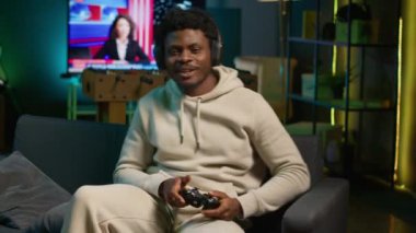 Afrika kökenli Amerikalı bir adam çatı katında video oyunu oynuyor, eğlence olsun diye kontrol cihazını tutuyor. Erkek oyuncu geceleri internet çok oyunculu oyunlara katılıyor. Kamera A.
