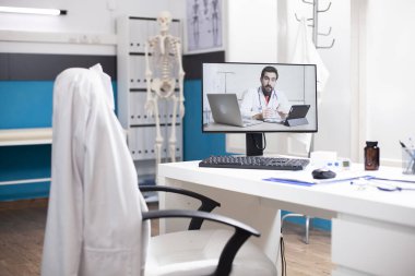 Kafkas doktor görüntülü arama masaüstü bilgisayarında gösterildi boş hastane ofisinin masasında. Bilgisayar ekranı, sağlık uzmanının sanal tıbbi danışmanlık yaptığını gösteriyor..