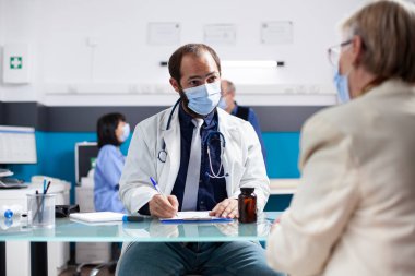 Kafkasyalı doktor yaşlı bir hastayla birlikte sağlık muayenehanesinde oturur ve muayene sırasında tedavileri dikkatlice tartışır. Emekli hasta kadın semptomlarından bahsederken erkek doktor panoya şöyle yazmış:.