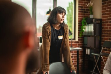 Caucasian lady sharing her mental health struggles with attentive aa community, speaking openly in cozy, brick wall therapy office. Young woman standing in room, seeking support in counseling program. clipart