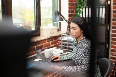 Pencere kenarındaki kadın araştırmacı titizlikle pazarlama analizlerini güncelliyor. Asyalı kadın masasındaki proje güncellemelerine odaklanıyor. Modern bir çalışma alanında bilgisayarında çalışıyor..