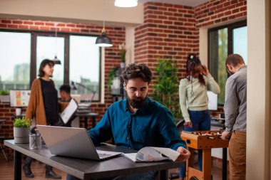 Masasında oturan beyaz bir mali danışman elinde kağıtlarla dizüstü bilgisayarına analitik girdi. İş adamı, araştırma belgelerini ve kişisel bilgisayarındaki bilgileri inceliyor.