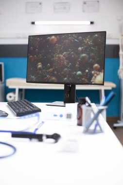 Boş hastane odasındaki dijital ekranda mikroskobik mikroplar sergileniyor ve sağlık sektöründeki virüs araştırmalarına odaklanıyor. Doktorların masası, hastalığa tıbbi tepkiyi yansıtan kurulum.