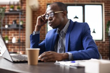 Girişimci, ofis masasında dizüstü bilgisayarla oturur ve iş projesini değerlendirir. Siyah erkek analist, dijital cihazdaki pazarlama stratejisi sunumunu incelerken şaşkına dönmüş ve nefes veriyor..