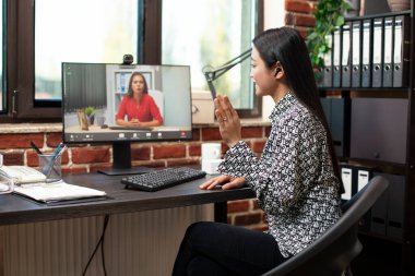 Kadın çalışan web kamerasına doğru el sallıyor, uzaktaki meslektaşını modern ofiste sanal bir toplantı sırasında selamlıyor. İş kadını potansiyel bir müşteriyle video konferans görüşmesinde selam veriyor..