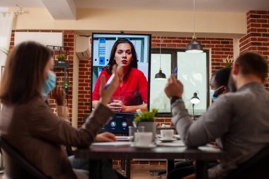 İş arkadaşları dijital ekranı kullanarak video konferans sırasında uzak bir bayan istemciyle başlangıç projesini tartıştılar. Çeşitli ekipler sanal görüşme için kadın analistle işbirliği yapar, toplantı odasında tartışırlar..
