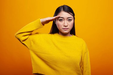 Sarı kazaklı genç bir kadın, kameraya ciddi bir ifadeyle bakıyor, onur ve vatanseverlik saçıyor. Saygı gösteren bir yetişkin kadın. Alnına elini koydu..