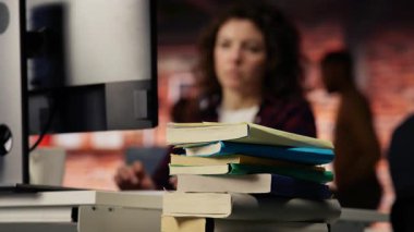 Başlangıç bürosu masasında PC 'de yazan, görevleri çözen bulanık arkaplanlı bir kadınla kitap yığınına odaklan. Girişim şirketinin çalışma alanındaki yığınla kitap. Çalışanların önünde, kamera B kapanıyor.
