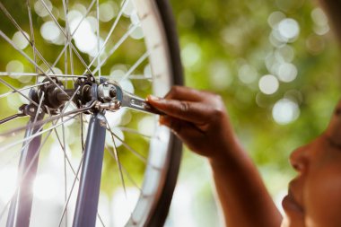 Görüntü, bisiklet merkezi ve dingilde özel anahtar kullanan genç siyahi bir kadının yakın çekimini gösteriyor. Açık havada bisiklet tekerleğini sıkan Afrikalı Amerikalı 'nın detaylı görüntüsü..