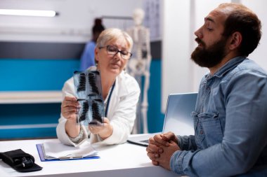 Yaşlı hekim hastanede sakallı bir adamla oturmuş elinde röntgen görüntüsü tutuyor ve radyoloji bulgularını açıklıyor. Emekli kadın doktor ve genç erkek hasta klinikte akciğer radyografisi hakkında tartışıyorlar..
