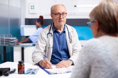 Yaşlı erkek doktor, hastane konsültasyonu sırasında kaygısına dikkat çeken emekli kadın hastayla sağlık tedavi seçeneklerini tartışıyor. Kıdemli doktor emekli bir kadına danışmanlık yapıyor..