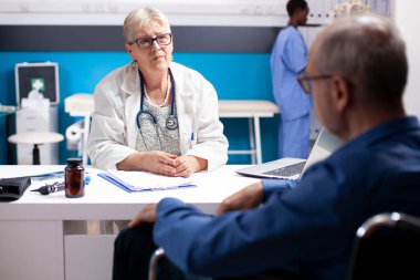 Klinik randevusu sırasında yaşlı bir adamın sağlık sorunlarını dinleyen yaşlı kadın doktorlara odaklanın. İlgili kıdemli hekim, emekli erkek hastaya tıbbi tavsiyelerde bulunur.