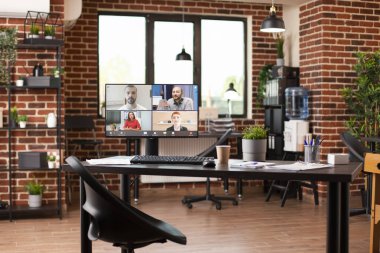 Boş tuğla ofis, meslektaşlarını görüntülü konferansta gösteren bir masaüstü ekrana sahip. Rafların, kapalı tesislerin, su dağıtıcının ve devam eden sanal toplantıları gösteren bilgisayarın bulunduğu iyi düzenlenmiş bir oda..