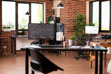 Ekranda şirket büyüme sunumuyla birlikte bilgisayar içeren boş ama davetkâr çalışma alanı. Tuğla duvar odası modern mobilya, canlı bitkiler ve içecek için langırt masasıyla döşenmiştir..