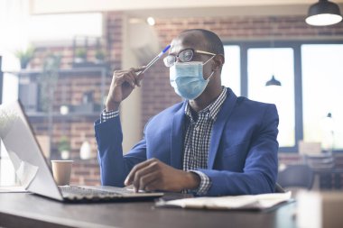 Masada oturan Afrikalı Amerikalı adam elinde kalemle başlangıç analizlerine odaklanmış. Tuğla duvar ofisindeki siyah erkek yönetici alnına hafifçe vuruyor ve dizüstü bilgisayarında yeni iş projeleri yapıyor..