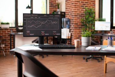 Başlangıç ofisindeki boş masa veri analizini gösteren, teknolojinin kesin sonuçlar için kullanımını vurgulayan bir bilgisayar barındırıyor. Tuğla duvar odası, çalışma alanı malzemeleriyle iyi düzenlenmiş..