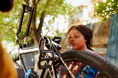 Sağlıklı, Afro-Amerikan bayan bisikletçi modern bisiklet pedalları ve zincirleri üzerinde her yıl ayar yapıyor. Genç siyah kadın dışarıda eğlenmek için bisiklet parçalarını titizlikle inceliyor.