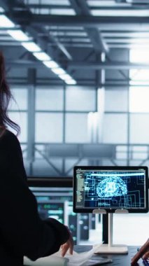 Dikey Veri Merkezi ekibi sunucu odasındaki belgeleri inceliyor, tabletteki yapay zeka kullanarak sistem raporlarını analiz ediyor. Yapay zeka sunucu odası yöneticileri mali belgelere bakıyor, kamera B