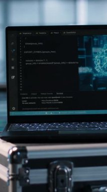 Veri merkezi mühendislerinin önünde arka planda suni zeka araçları yerleştiren dikey video dizüstü bilgisayar. Not defteri ekranındaki yapay zeka kodlaması sunucu kümelerini inceleyen teknisyenlerin yanında, kamera A