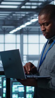 Sunucu çiftliğinde çalışan teknisyenlerden oluşan dikey video ekibi verileri analiz etmek için dizüstü bilgisayar kullanıyor. Veri merkezindeki altyapıyı inceleyen ekip çalışanları, sistem bütünlüğü ve güvenliğinin sağlanması, kamera B