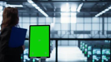 Bulanık geçmişi olan teknisyenlerin önünde sunucu çiftliğinde veri analiz eden izole ekran modelleme tableti. Krom anahtar tabletini veri merkezini inceleyen iş arkadaşlarının yanına kapat, kamera B