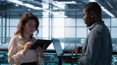 Veri merkezinde dizüstü bilgisayar kullanan gülümseyen yöneticiler, sunucu viralizasyonunu yönetiyorlar. Neşeli bilişim uzmanı ve Afro-Amerikan adam sunucu odasında not defteri kullanıyor, altyapı güvenilirliğini sağlıyorlar, kamera A