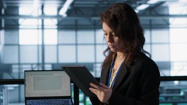 Veri merkezindeki teknisyen, tablet entegre yapay zeka ile çalışan otomasyon araçları, öngörücü bakım rutinleri çalıştırıyor. Sunucu odasının sürekli güncellenmesini sağlayan kadın, veri akışını yöneten, kamera A
