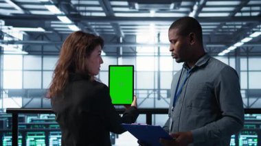 Veri merkezindeki bilgisayar bilimcileri taklit tablet kullanıyor, sunucu donanımlarını denetliyor, cihazları güncelliyor. Krom anahtar aygıtı, kamera B kullanılarak dengeli işlemleri sağlamak için işbirliği yapan bilişim iş arkadaşları