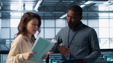 Bilgi işlem uzmanlarından oluşan bir ekip veri merkezi kontrol listesi evraklarını inceliyor. Afrikalı Amerikalı adam ve iş arkadaşı sunucu çiftliğinde işbirliği yapıyor. Belge dosyaları, kamera A