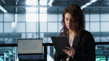 Yeni sunucu mimarileri yerleştirmek için tablet üzerinde yapay zeka teknolojisi kullanan veri merkezinde yönetici. Sunucu odasındaki kadın sabit performansı korumak için depolama sıralarını güncelliyor, kamera A