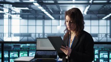 Yeni sunucu mimarileri yerleştirmek için tablet üzerinde yapay zeka teknolojisi kullanan veri merkezinde yönetici. Sunucu odasındaki kadın sabit performansı korumak için depolama dizilerini güncelliyor, kamera B