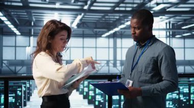 Veri merkezi yöneticileri evrak dosyalarını okuyor, sistem tanılarını gözden geçiriyorlar. Sunucu odası çalışanları bakım programı belgelerini ve siber güvenlik protokollerini inceliyor.