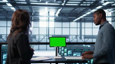 Veri merkezi ekibi yeşil ekran tableti kullanıyor evrak dosyalarını ve güvenlik protokollerini inceliyor. Kritik sistem raporlarını analiz eden kroma anahtar cihazının yanındaki sunucu odası adresleri, kamera B