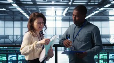 Bilgi işlem uzmanlarından oluşan bir ekip veri merkezi kontrol listesi evraklarını inceliyor. Afrikalı Amerikalı adam ve iş arkadaşı sunucu çiftliğinde işbirliği yapıyor. Belge dosyaları, kamera B