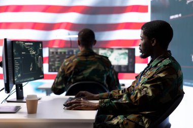Amerikan askeri üniformalı istihbarat memurları bir komuta merkezinde bilgisayar üzerinde çalışıyor, gözlem ve veri analizini yönetiyorlar. ABD hükümeti için küresel operasyonları destekle.