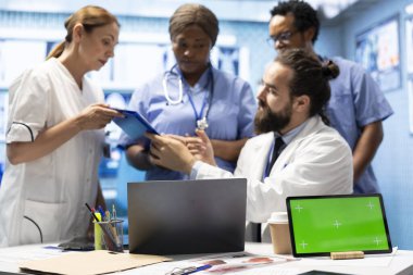 Doktorlar ve hemşireler radyografi taramalarını masasında yeşil ekranla inceleyerek özel klinikteki potansiyel teşhis ve tedavi planlarını tartıştılar. Profesyonel uzmanlar uzmanlıkla çalışırlar..
