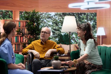 Ev ziyareti sırasında tekerlekli sandalyedeki yaşlı kadına danışmanlık yapan sosyal hizmetler görevlisi, iyileşme tedavisi ve sağlık takviyeleri hakkında konuşuyor. Hemşire kıdemli destek ve tavsiye sunar.