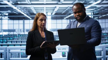 İş arkadaşları, veri merkezi ekipman ömrünü uzatmak için tablet ve laptop kullanarak yıllık bakım yapıyorlar. Sunucu merkezindeki yönetici ekibi dijital aygıt, kamera B kullanarak süper bilgisayarları izliyor.