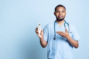 Afrika kökenli Amerikalı hemşire, hastaların vücut ısılarını ölçmek için aksesuar kullanarak, ateş seviyelerini ölçmek için termometre reklamı yapıyor. Stüdyoda erkek tıp asistanı..