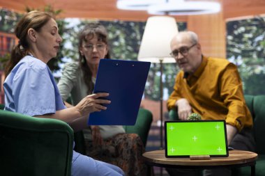 Yaşlı bir adam ve kadın evlerinde yeşil ekranlı bir tabletle hemşirelerle konuşuyor, eğlenceli bir sohbet ediyorlar ve rehberlik istiyorlar. Yaşlı çift iyi hissediyor, check-up ziyareti sırasında dinleniyorlar..