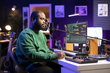 Besteci yeni şarkıya uyacak yeni kafiyeler düşünüyor, kendi stüdyosunda bir şarkı üretmek için mısralar yazıyor. Profesyonel söz yazarı ilk albümü için müzik yapıyor..