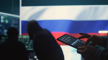 Devlet siber güvenlik odasında Rus bayrağı altında çalışan kişi tablet kullanıyor. Siber tehditler savurmak, izinsiz giriş yapmak ve sahte haberler yaymak için sistemlere sızmak. Kapatın. Kamera B.