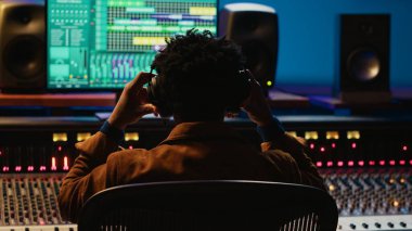 Profesyonel takip mühendisi kayıt odasındaki ses kontrol düğmelerini düzenlemek için kulaklık kullanıyor. Konsol ve yazılımı karıştırma üzerine çalışan bir ses uzmanı. Kamera A.