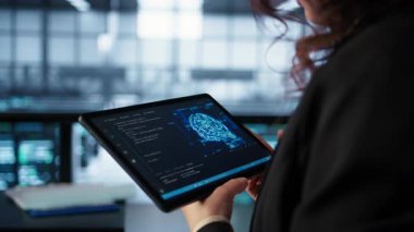 Veri merkezi teknisyeni savunmasızlığı önlemek için tablet üzerinde yapay zeka kullanıyor. Çalışan güvenlik duvarı kurallarını gözden geçirmek için aygıt kullanıyor, yapay zeka siber güvenlik protokollerini uyguluyor, kamera B kapatıyor.