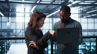 Veri merkezindeki geliştiriciler dizüstü bilgisayarda kodlama, ölçümleri analiz etme, depolama hacmini optimize etme. Bilgi işlem uzmanları sunucu odasında dizüstü bilgisayar kullanarak, sorunsuz işlemler ve kamera B ile çalışıyorlar.