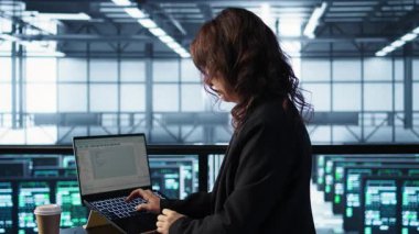 Veri merkezindeki yönetici depolama dizilerini güncellemek için dizüstü bilgisayar kullanarak ağ viralizasyonunu yapılandırıyor. Sunucu odasında elinde kahve fincanı tutan bir kadın, sabit performans için ayarları doğrulayan, kamera B