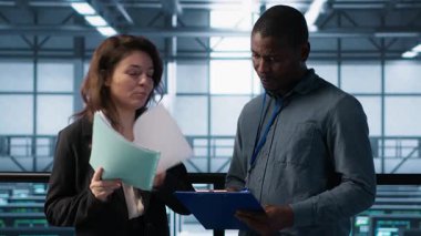 Veri Merkezi yöneticileri evrak dosyalarını okuyor, sistem tanılarını gözden geçiriyorlar. Sunucu çiftliği meslektaşları bakım takvimlerini evrakları ve siber güvenlik protokollerini inceliyor, kamera A