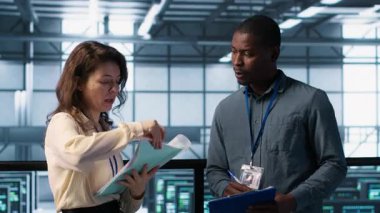 Veri merkezi ekibi yüksek teknoloji sunucu odasındaki evrak dosyalarını inceliyor. Kritik sistem raporlarını ve güvenlik protokollerini inceliyor. Mali belgelere bakan sunucu odası yöneticileri, kamera A