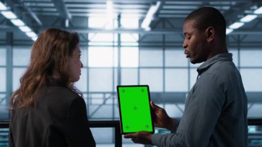 Sunucu odası veri bilimcileri taklit tablet kullanıyor, hataları önlemek için güvenlik denetimleri yapıyor. Veri merkezinde iş arkadaşı olan Afrikalı Amerikalı bir adam yeşil ekran cihazına bakıyor, kamera A