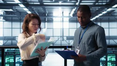 Veri merkezi ekibi yüksek teknoloji sunucu odasındaki evrak dosyalarını inceliyor. Kritik sistem raporlarını ve güvenlik protokollerini inceliyor. Mali belgelere bakan sunucu odası yöneticileri, kamera B